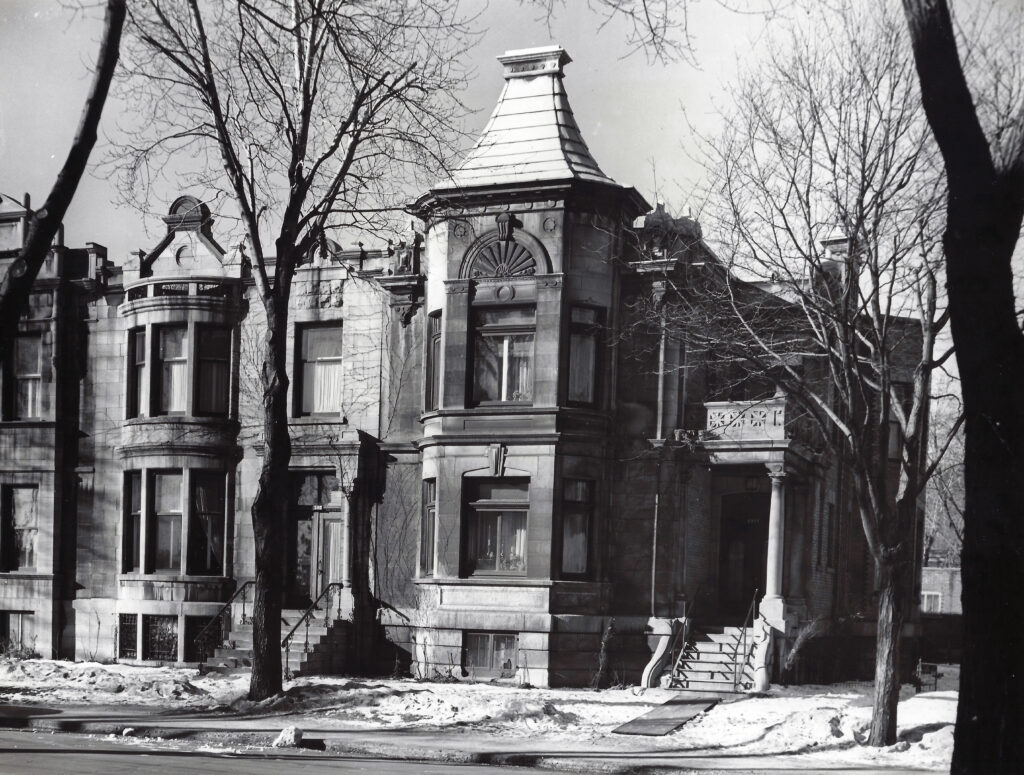 Photographie en noir et blanc d’un bâtiment historique en pierre situé au 4285 boulevard de Maisonneuve Ouest, ancien site d’hébergement du CSAI pour les femmes et enfants en difficulté entre 1947 et 1987. L’image montre une architecture élégante avec des façades détaillées, des escaliers menant aux entrées et des arbres dénudés en hiver.