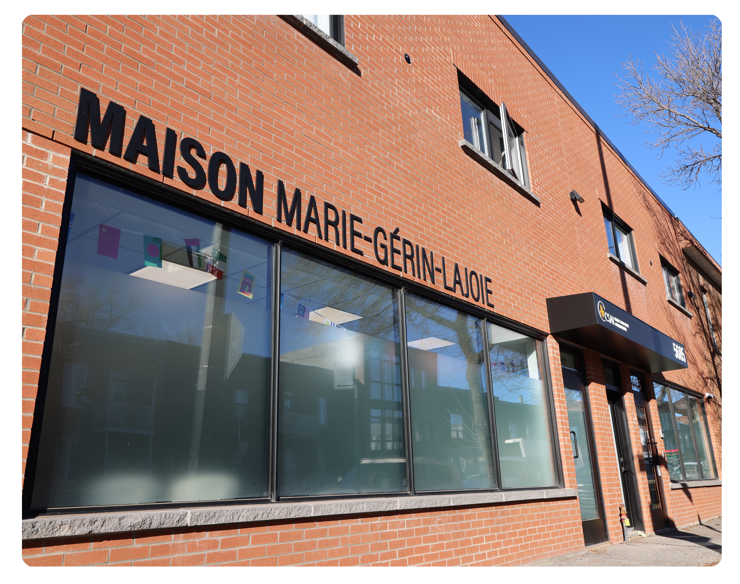 Façade de La Maison Marie-Gérin-Lajoie, un bâtiment en brique rouge avec de grandes fenêtres et une enseigne en lettres noires. Ce centre d’hébergement temporaire, géré par le CSAI, accueille les réfugiés pris en charge par l’État (RPCÉ) à Montréal.